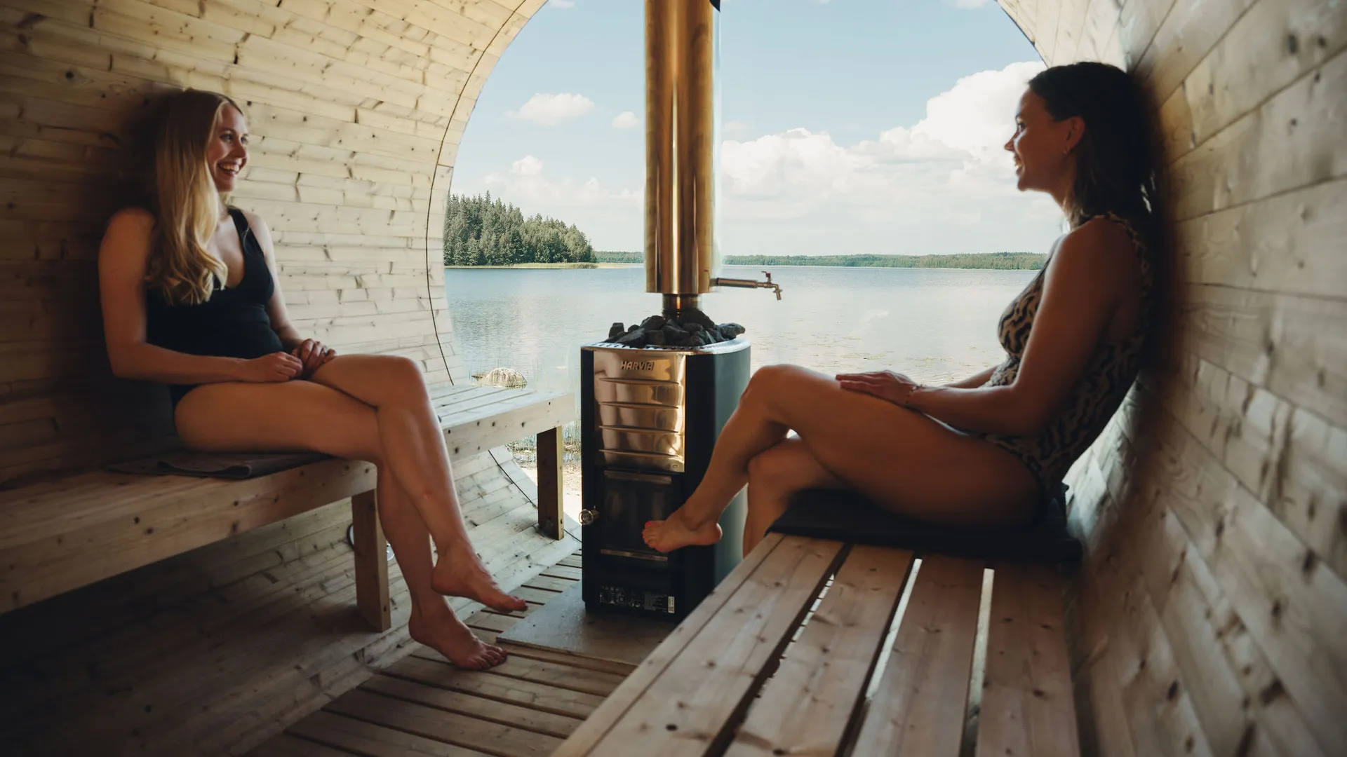 Two women in a sauna with a lake view.